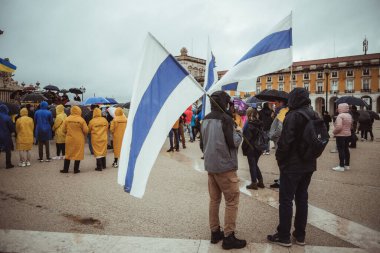 Lizbon, Portekiz - 20 Mart 2022: Ukrayna 'ya ve Rus işgali ve savaşına karşı bir protesto eylemi: savaş karşıtı mavi ve beyaz bayraklı bir grup protestocu anıt ve sahnenin yanında