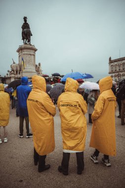 Lizbon, Portekiz - 20 Mart 2022: Rus işgali ve savaşına karşı Ukrayna 'yı desteklemek için eylem: Sahne önünde ve anıtın önünde sarı yağmurluklu üç protestocu