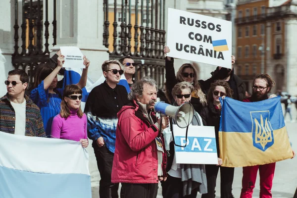 Lizbon, Portekiz - 13 Mart 2022: Rus askeri saldırganlığını ve savaşını protesto etmek: Lizbon meydanında elinde posterler ve bayraklar olan insanlar, bir konuşmacı megafon kullanıyor