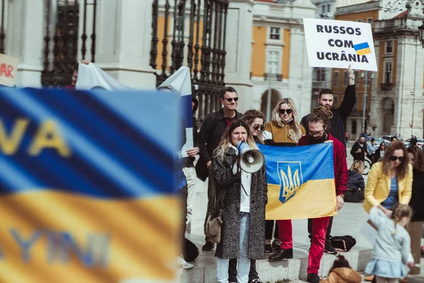 Lizbon, Portekiz - 13 Mart 2022: Rus askeri saldırganlığını ve savaşını protesto: Lizbon meydanında elinde posterler ve Ukrayna bayrakları olan insanlar, megafonlu bir kadın