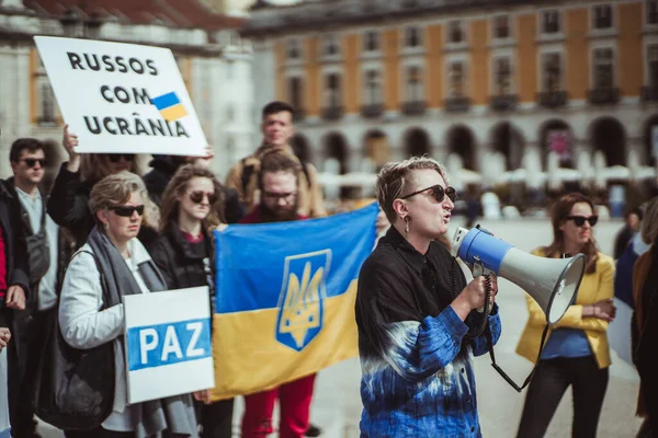 Lizbon, Portekiz - 13 Mart 2022: Rus askeri baskını ve savaşa karşı protesto yürüyüşü: Lizbon 'un ana meydanında elinde posterler ve Ukrayna bayrakları olan insanlar, bir kadın megafon kullanıyor