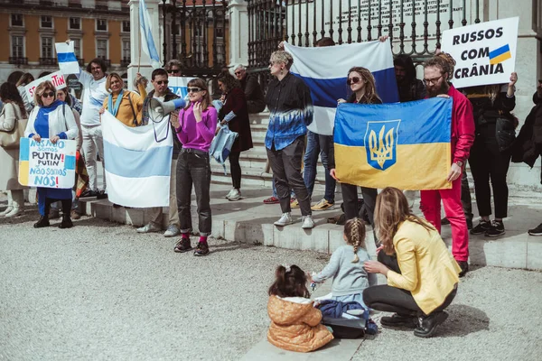 Lizbon, Portekiz - 13 Mart 2022: Rusya 'nın Ukrayna' ya saldırısına karşı protesto yürüyüşü: Lizbon 'un ana meydanında posterleri ve bayrakları olan protestocular; ön planda iki çocuk ve anneleri