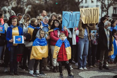 Lisbon, Portugal - April 20, 2022: two little boys standing in the sqaure surrounded by Ukranian protesters during a protest rally against the Russian invasion dedicated to saving the city of Mariupol