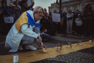 Lisbon, Portugal - April 20, 2022: protest rally dedicated to saving the Ukrainian city of Mariupol from the Russian aggression; women wrapped in Ukrainian flags lighting candles in memory of the dead