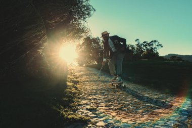 Orta yaş krizindeki komik siyah bir adamın silüeti. Hasır şapkalı ve güneş gözlüklü şık bir takım elbise giyiyor. Gün batımında kaldırım taşında elinde golf sopasıyla uzun bir tahta üzerinde geziyor.