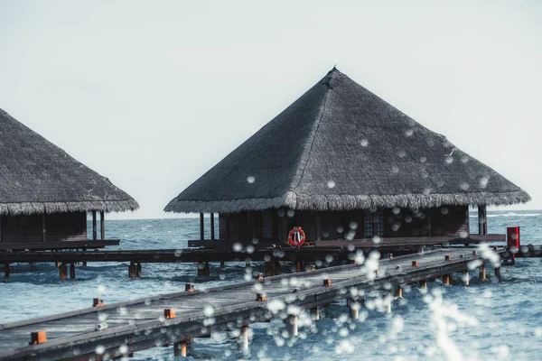 马尔代夫旅游胜地典型的豪华三角村舍景观 有三角形的天篷屋顶和人行横道的码头或有水花的桥 在一个阳光灿烂的暖和的天气里 前景一片混乱 — 图库照片