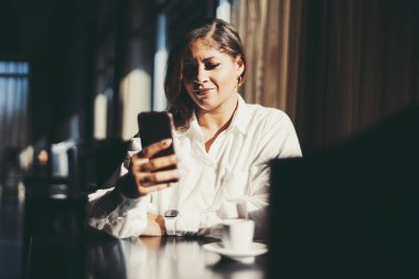 Lokantanın karanlık bir köşesinde oturan ve akıllı telefonunu kullanarak cevap veren iri yarı bir İspanyol iş kadınının portresi masanın yanında bir fincan espresso kahvesi.