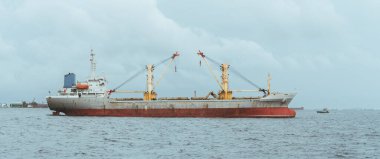 Okyanustaki dev bir Türk yük gemisinin panoramik bir görüntüsü üzerinde iki kargo vinci olan ana adadan çok da uzak olmayan erkek sularında büyük bir kargo gemisi, sıcak ve bulutlu bir gün.