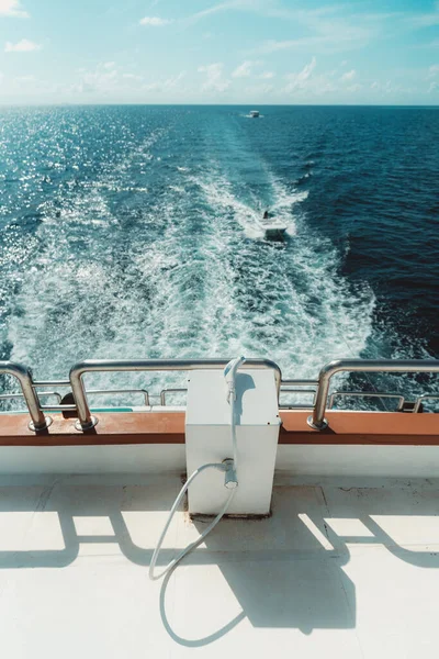 A vertical wide-angle shot of a small auxiliary shower on the upper deck of a sailing diving safari yacht with a teal ocean with two more vessels in a defocused background