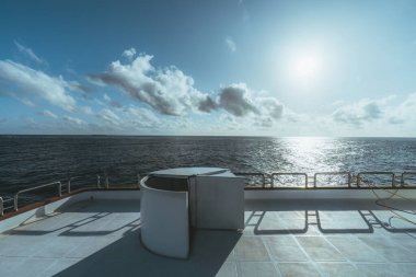 Lüks bir safari yatının üst güvertesinden geniş açılı bir çekim. Alt güverteden orta güverteye kadar uzanan bir safari yatı. Deniz manzarası, bulutlar ve krom eskrimden yansıyan sıcak bir güneş gölgesi.