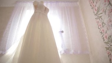 Gelinlik bir mankene asılıyor ve odanın penceresinden güneş ışınlarıyla aydınlatılıyor..