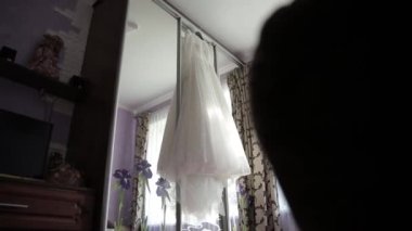 Gelinlik, aynalı kapısı olan sürgülü bir gardıroba asılı.