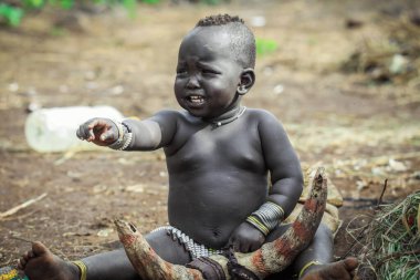 Omo Nehri Vadisi, Etiyopya, Kasım 2020, Mursi kabilesinden küçük bir çocuk yerde oturuyor.