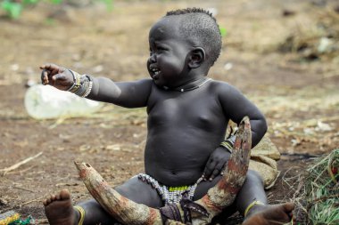 Omo Nehri Vadisi, Etiyopya, Kasım 2020, Mursi kabilesinden küçük bir çocuk yerde oturuyor.