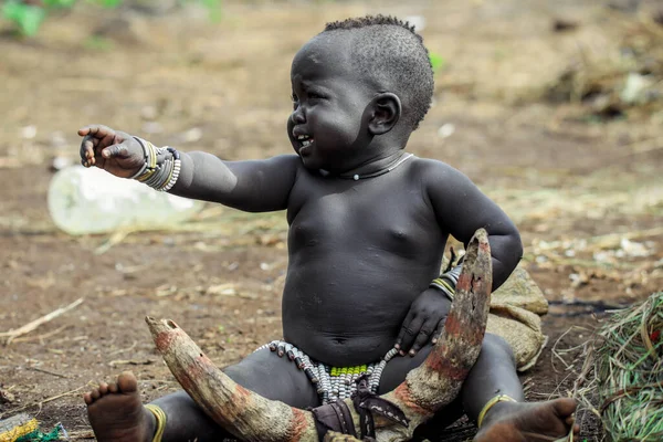 Omo Nehri Vadisi, Etiyopya, Kasım 2020, Mursi kabilesinden küçük bir çocuk yerde oturuyor.