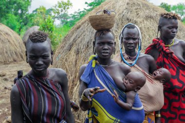 Omo Nehri Vadisi, Etiyopya - 29 Kasım 2020: Parlak elbiseli tüm kadınlar Mursi kabile köyündeki turistlere poz veriyor