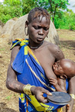 Omo Nehri Vadisi, Etiyopya, Kasım 2020, Mursi kabilesi köyünde mavi ve sarı elbiseli bir bebek.