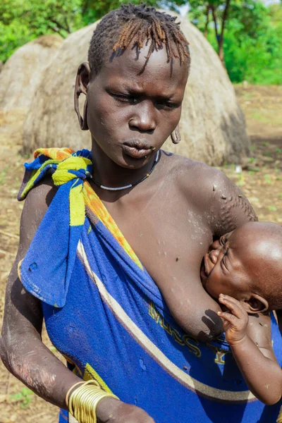 Omo Nehri Vadisi, Etiyopya, Kasım 2020, Mursi kabilesi köyünde mavi ve sarı elbiseli bir bebek.