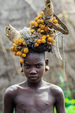 Omo Nehri Vadisi, Etiyopya - 29 Kasım 2020: Geleneksel tahta küpeli Afrikalı Gençlerin Portresi ve Mursi kabile köyünde başında kuru sarı çiçekler olan Kırık Boynuzlar