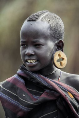 Omo Nehri Vadisi, Etiyopya - 29 Kasım 2020: Yerel Mursi kabile köyünde Haçlı haçları olan büyük ve geleneksel tahta küpeli Afrikalı Genç Çocuğun Portresi