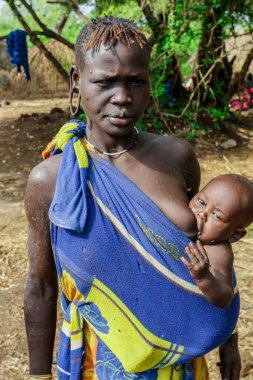 Omo Nehri Vadisi, Etiyopya, Kasım 2020, Mursi kabilesi köyünde mavi ve sarı elbiseli bir bebek.