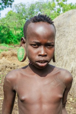 Omo Nehri Vadisi, Etiyopya - 29 Kasım 2020: Yerel Mursi kabilesi köyünde büyük ve geleneksel ahşap küpeli Afrikalı bir gencin portresi)