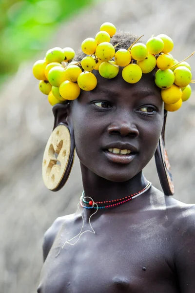 エチオピアのオモ川渓谷 2020年11月29日 地元のムルシ族の村で頭の上に大きな伝統的な木製のイヤリングと乾燥した黄色の花の花輪を持つアフリカのティーンエイジャーの肖像画 編集のみを使用します — ストック写真