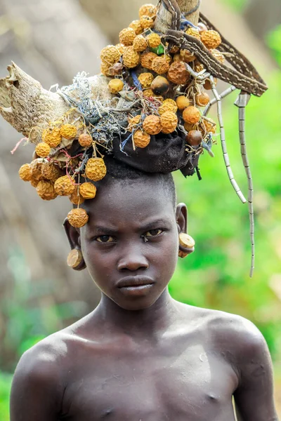 エチオピアのオモ川渓谷 2020年11月29日 アフリカの10代の肖像画で 丸い伝統的な木製のイヤリングと壊れた角と乾燥した黄色の花がムルシ族の村の頭の上にあります — ストック写真