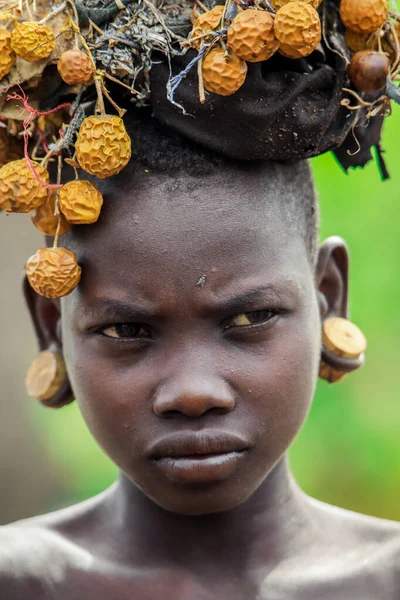 エチオピアのオモ川渓谷 2020年11月29日 地元のムルシ族の村で頭の上に大きな伝統的な木製のイヤリングと乾燥した黄色の花の花輪を持つアフリカのティーンエイジャーの肖像画 編集のみを使用します — ストック写真