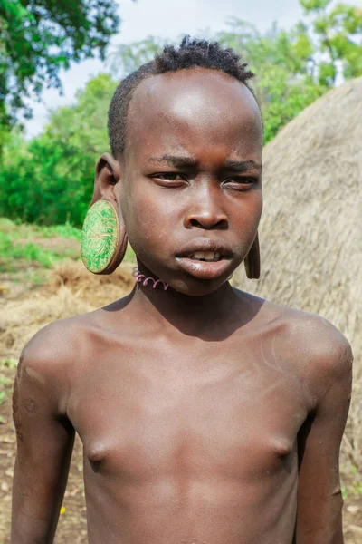 Omo Nehri Vadisi, Etiyopya - 29 Kasım 2020: Yerel Mursi kabilesi köyünde büyük ve geleneksel ahşap küpeli Afrikalı bir gencin portresi)