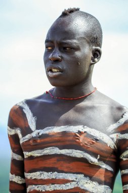 Omo Nehri Vadisi, Etiyopya - 29 Kasım 2020: Mursi kabilesi köyünde boyalı vücutlu genç Afrikalı adamın portresi
