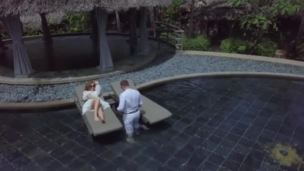 一对恋人穿着白衣 躺在游泳池的日光浴床上 — 图库视频影像