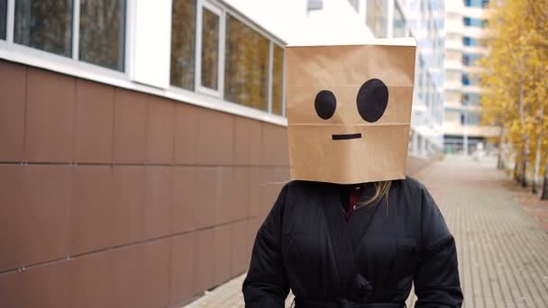 Onverstoorbare kalme krankzinnige papieren zak gezicht lopen langs straat. Vrouw draagt broodzak met emoticons — Stockvideo