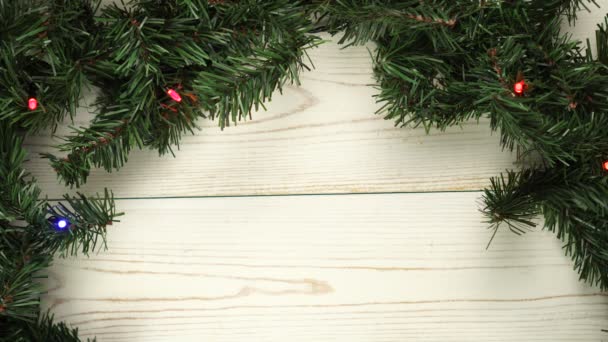 Fondo de madera blanca navideña con guirnalda luminosa y ramas de pino — Vídeos de Stock