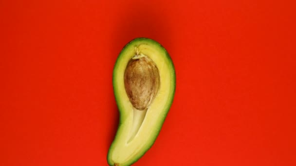 Draufsicht auf rotierende grüne Avocado, halbiert mit Grube auf rotem Hintergrund. — Stockvideo