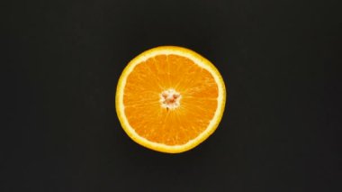 Siyah arka planda turuncu dönüyor. Taze meyve suyu, meyve, vitamin ve yaz konsepti. Sulu bir turunçgilin üst görüntüsü