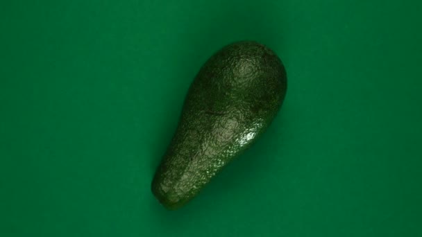 Цілий фрукт авокадо обертається на зеленому фоні . — стокове відео