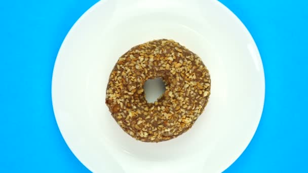 Top View Περιστρεφόμενο ντόνατ καλυμμένο με σοκολάτα Frosting με καφέ στροβιλίσματα σε λευκό πιάτο σε μπλε φόντο — Αρχείο Βίντεο