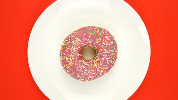 Яркий и красочный разбрызгиваемый пончик крупным планом медленно вращающийся на цветной белой тарелке. Вид сверху. Бесшовная петля. — стоковое видео