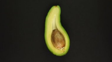 Olgun ve organik kesilmiş avokado siyah bir zemin üzerinde dönüyor.