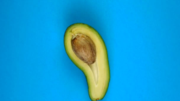 Mezzo frutto di avocado che ruota sul tavolo blu. L'avocado è un frutto altamente nutriente. Filmati in loop — Video Stock