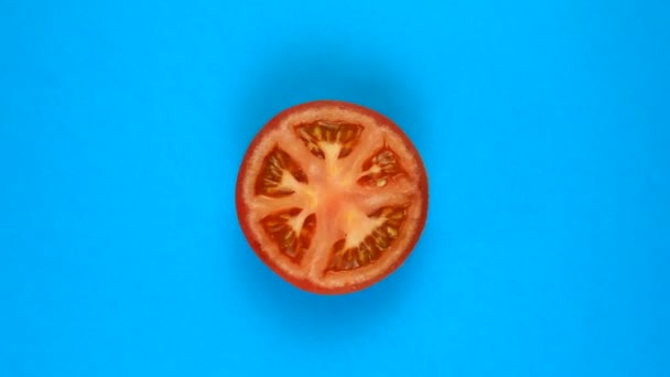 TOP VIEW: Halva tomaten roterar på en blå yta - snabb rörelse — Stockvideo