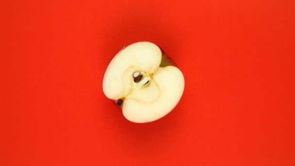 VER ARRIBA: La mitad de una manzana gira sobre una superficie roja: cámara lenta — Vídeos de Stock