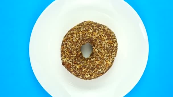 Donut de chocolate doce assado rapidamente girando em um prato. Isolado em azul, vista superior — Vídeo de Stock