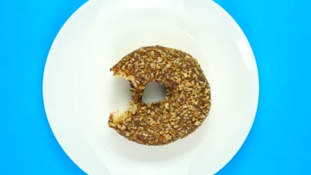 Eating fresh chocolate donut on blue background. Donat rotating. Top view. — Stock Video