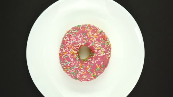 Fresh sweet donut rotating on a plate. Top view. Bright and colorful sprinkled donut close-up macro shot spinning on a black background — Stock Video