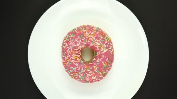 Tatlı pembe donut tabakta döner. Siyah üzerine izole edilmiş, üst görünüm — Stok video
