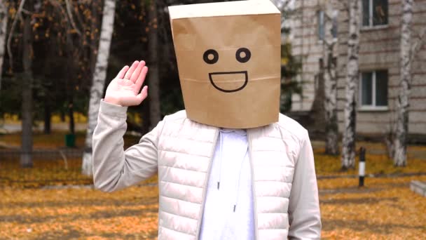 Smiling man wearing paper bag with happy emotion, man in mask standing outdoor and waving his hand for greeting someone — Stock Footage Smiling man wearing paper bag with happy emotion, man in mask standing outdoor and waving his hand for greeting someone Video Clip