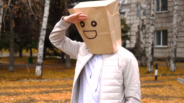 Smiling man wearing paper bag with happy emotion, man in mask standing outdoor and looking far away — Stockvideo