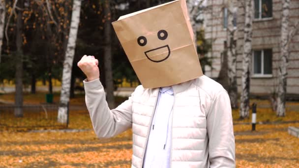 Sonriente hombre usando bolsa de papel con emoción feliz, hombre con máscara de pie al aire libre y amenazando su puño — Vídeo de stock